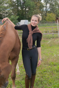 Woman in equestrian attire standing next to a horse in an outdoor setting