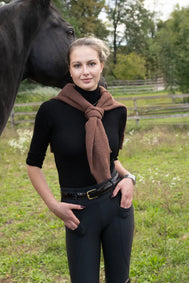 Woman in equestrian attire standing next to a horse in an outdoor setting