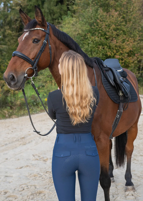 Woman in wearing Classy Equestrians high-rise riding tights standing next to a horse on a gravel path with trees in the background