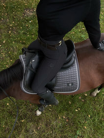 Close-up of a black leather saddle on a horse with grass in the background